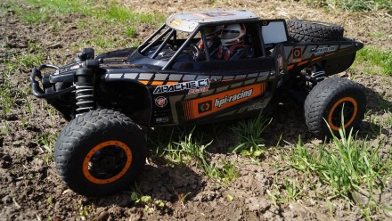 A black remote controlled car in muddy grass